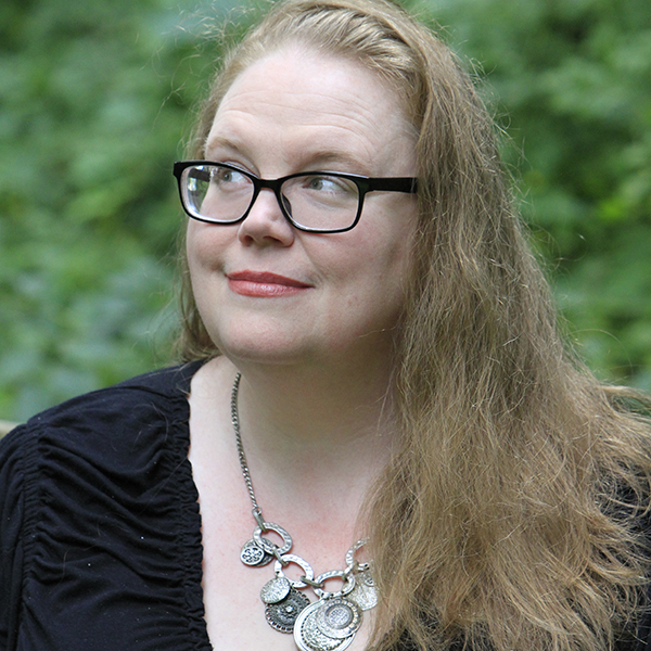 A headshot of Tammi Labrecque posed in front of a leafy green background. She is looking up and to the the right.
